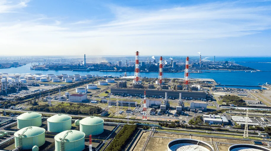 海沿いに立地する工場やプラントの空撮写真。複数のタンクや煙突が立ち並んでいる様子。